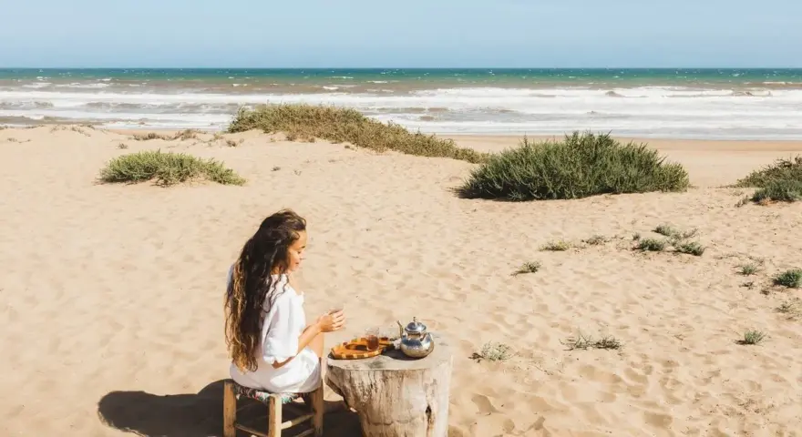 Kobieta pije herbatę na piaszczystych plażach Tunezji, z widokiem na ocean.