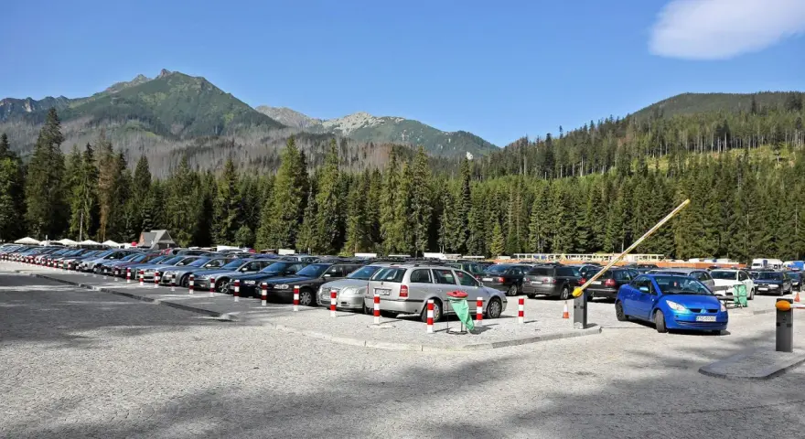 Parking przy wejściu na Morskie Oko. Rząd samochodów pod górskimi szczytami i gęstym lasem.