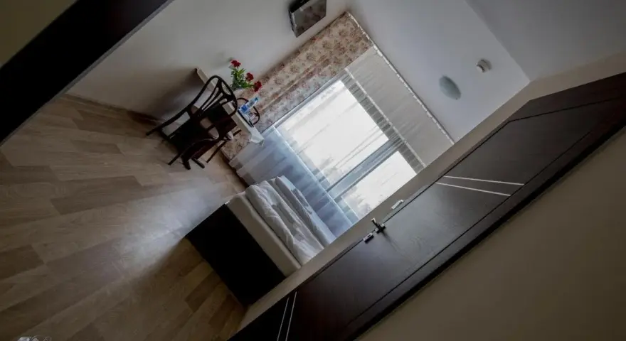 Pokój w hotelu i restauracji Crystal: łóżko, stolik z krzesłami i kwiatami, okno z zasłonami.