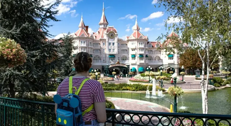 Dziewczyna z plecakiem w kształcie Myszki Miki podziwia zamek w Disneyland Paris. Bilety do parku już kupione, czas na przygodę!