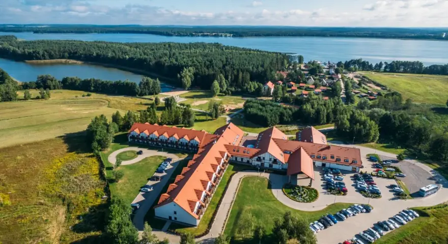 Malowniczy widok na Mikołajki Resort Spa z lotu ptaka, otoczony lasami i jeziorem. Idealne miejsce na relaks.