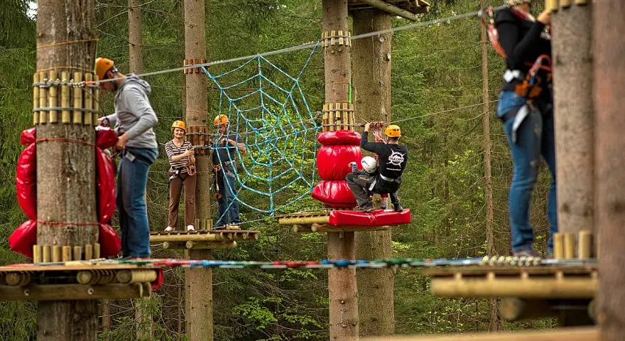 Park linowy Base Camp Istebna: ludzie na platformach wśród drzew, pokonują przeszkody, w tym pajęczynę.