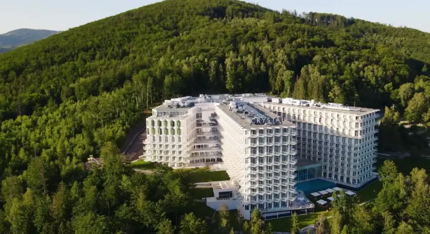 Nowy hotel w Wiśle, Crystal Mountain, wtopiony w zielone zbocze góry. Nowoczesna architektura z licznymi balkonami i basenem.