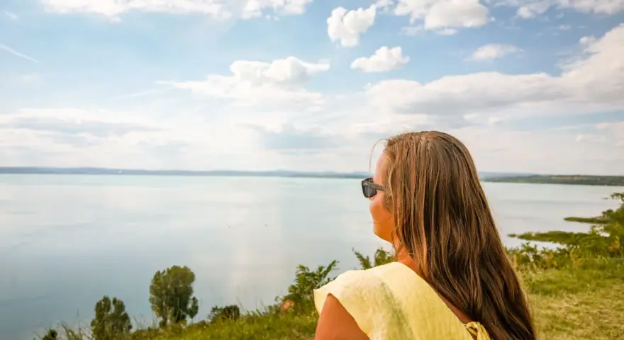 Kobieta w żółtej bluzce podziwia rozległe jezioro Balaton.