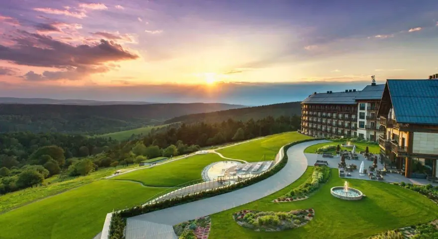 Hotel Arłamów z basenem i tarasem, otoczony zielonymi wzgórzami o zachodzie słońca. Ile pokoi ma hotel Arłamów? Tego nie widać, ale jest ich wiele!
