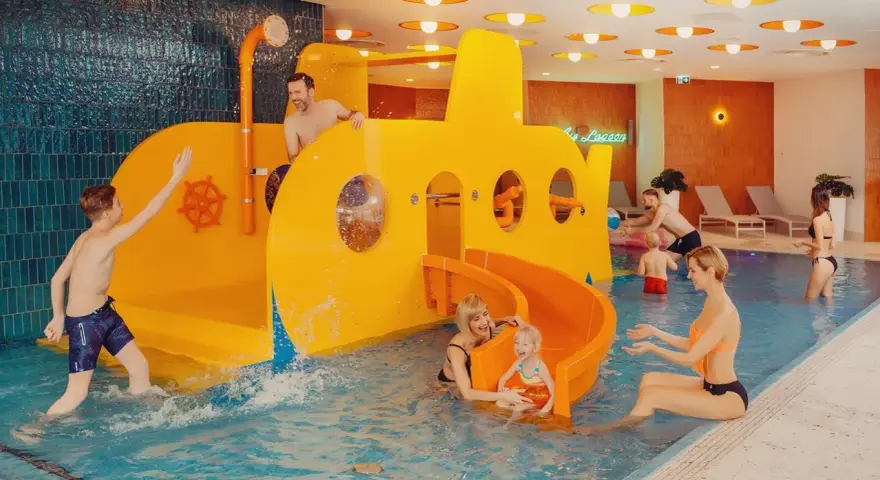 Rodzina bawi się w hotelu z aquaparkiem dla dzieci w górach. Żółta łódź podwodna ze zjeżdżalnią to centrum wodnych atrakcji.