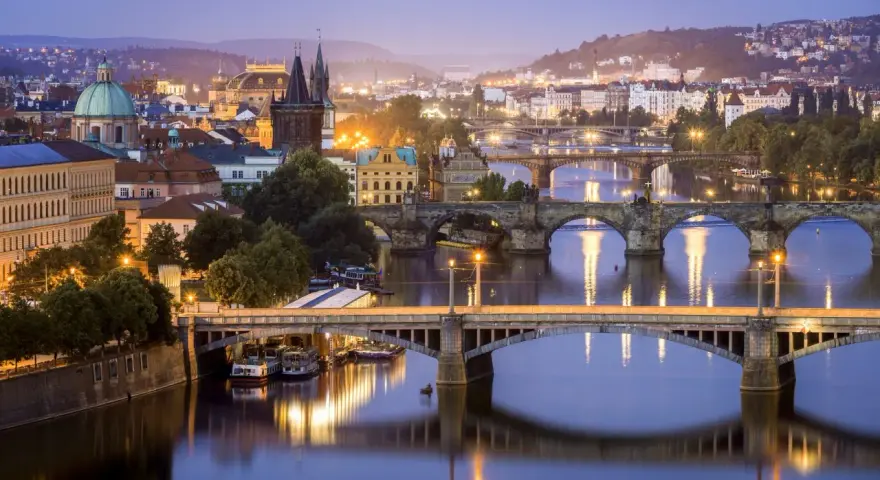 Praga nocą, z wieloma mostami na Wełtawie i oświetlonymi budynkami. Ciekawe ciekawostki o Czechach czekają na odkrycie w tym magicznym mieście.