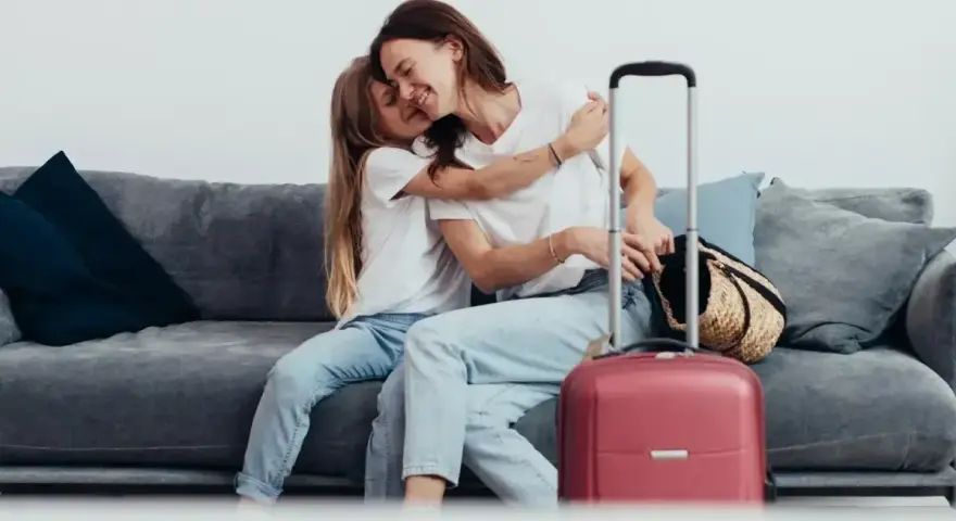 Mama i córka przytulają się na kanapie, obok walizka. Wszyscy, którzy chcą zameldować się w hotelu, mogą tu poczuć się jak w domu.