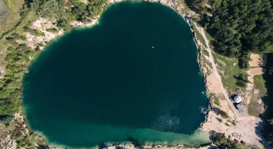 Serce polskiego balatonu, turkusowa woda, otoczona zielenią i piaszczystymi plażami. W oddali widać małą łódkę.