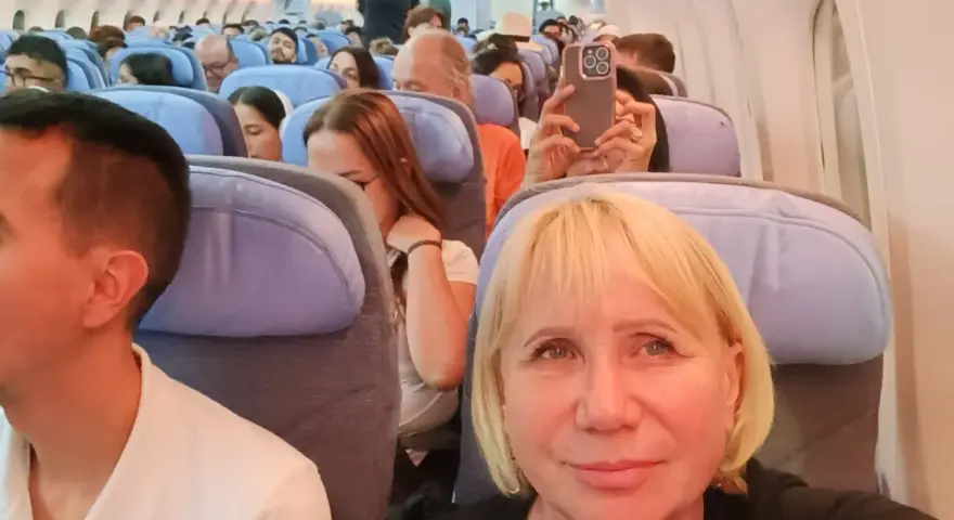 W samolocie, przygotowując się na najdłuższy lot samolotem, pasażerowie siedzą w rzędach. Kobieta robi zdjęcie telefonem.