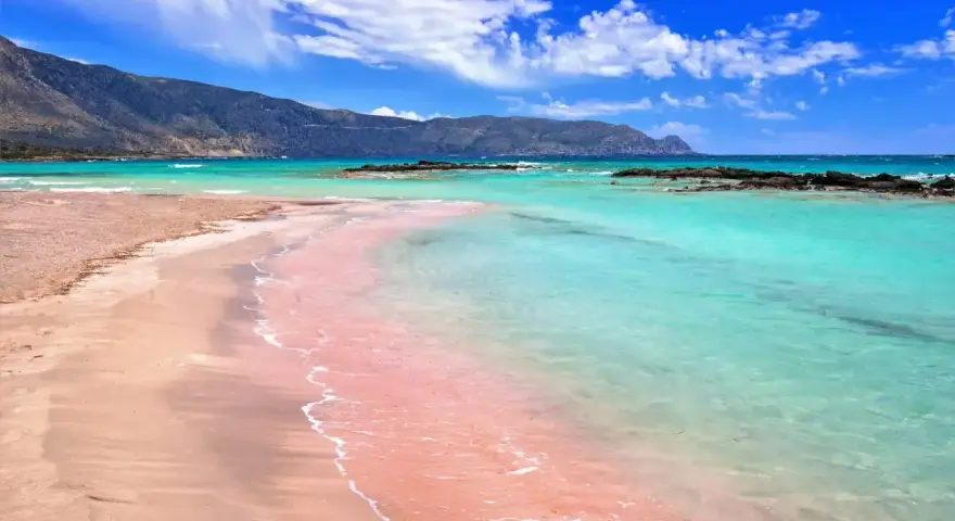 Różowa plaża Elafonisi z turkusową wodą i górami w tle. Idealne miejsce na relaks.
