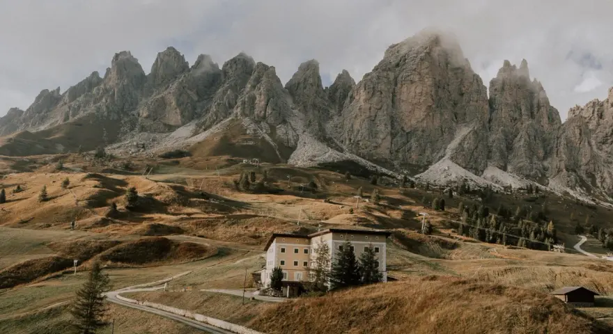 Malownicze **Val di Funes** z górami w tle, hotel na wzgórzu i kręta droga.