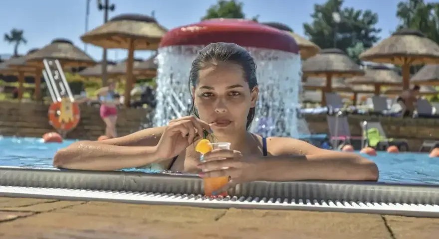 Kobieta w basenie z drinkiem, relaksująca się w słońcu. Idealny dzień all inclusive soft.