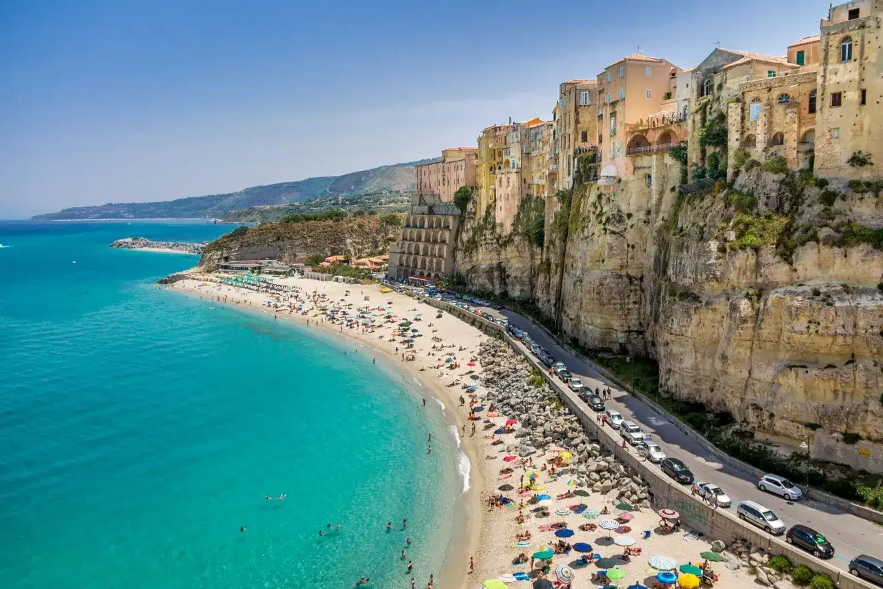 Tropea: malownicze miasteczko na klifie nad turkusowym morzem. Droga wzdłuż plaży z samochodami, jakby dojazd do tropea lotnisko był tuż obok.