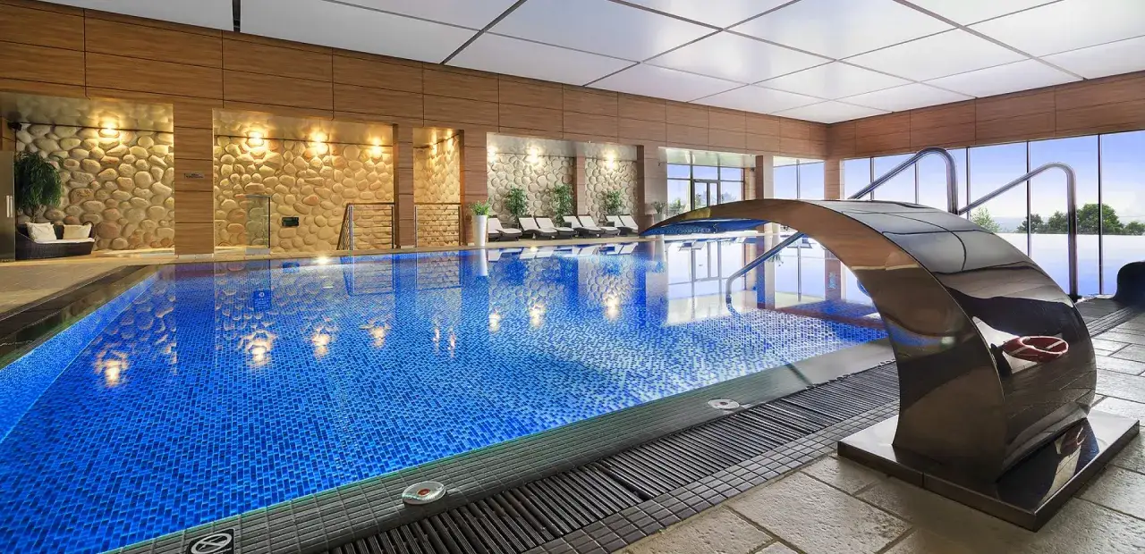 Luksusowy hotel z atrakcjami dla dorosłych: basen z wodospadem, leżaki i kamienne ściany tworzą relaksującą atmosferę.