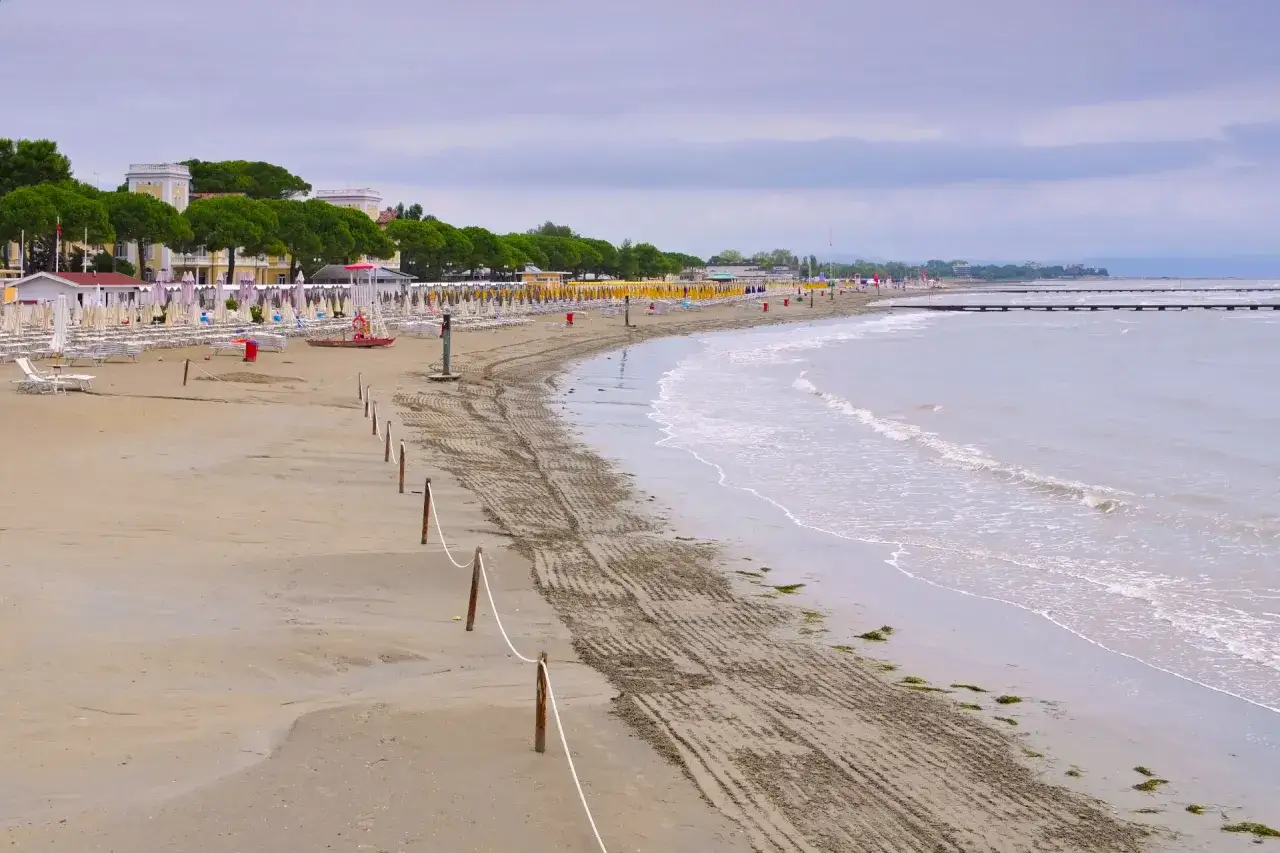 Pusta, szeroka triest plaża piaszczysta z rzędami leżaków i parasoli. Morze łagodnie faluje.