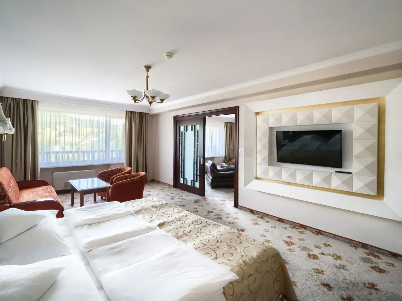 Pokój hotelowy z dwoma łóżkami, kanapą, fotelem i telewizorem. Ile pokoi ma Hotel Gołębiewski w Wiśle?