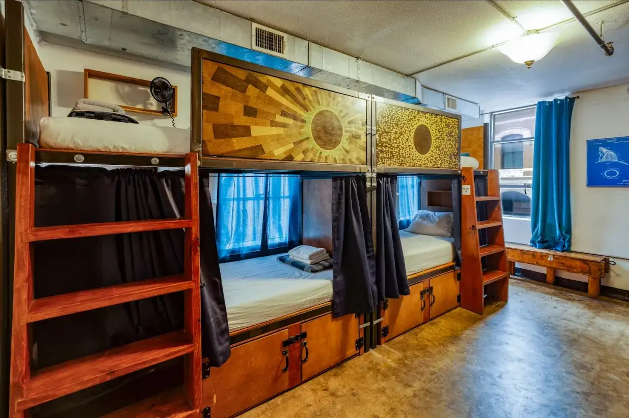 Wnętrze hostelu z łóżkami piętrowymi. Każde łóżko ma zasłonę, schowek i drabinę. To idealne miejsce dla podróżników szukających taniego noclegu.