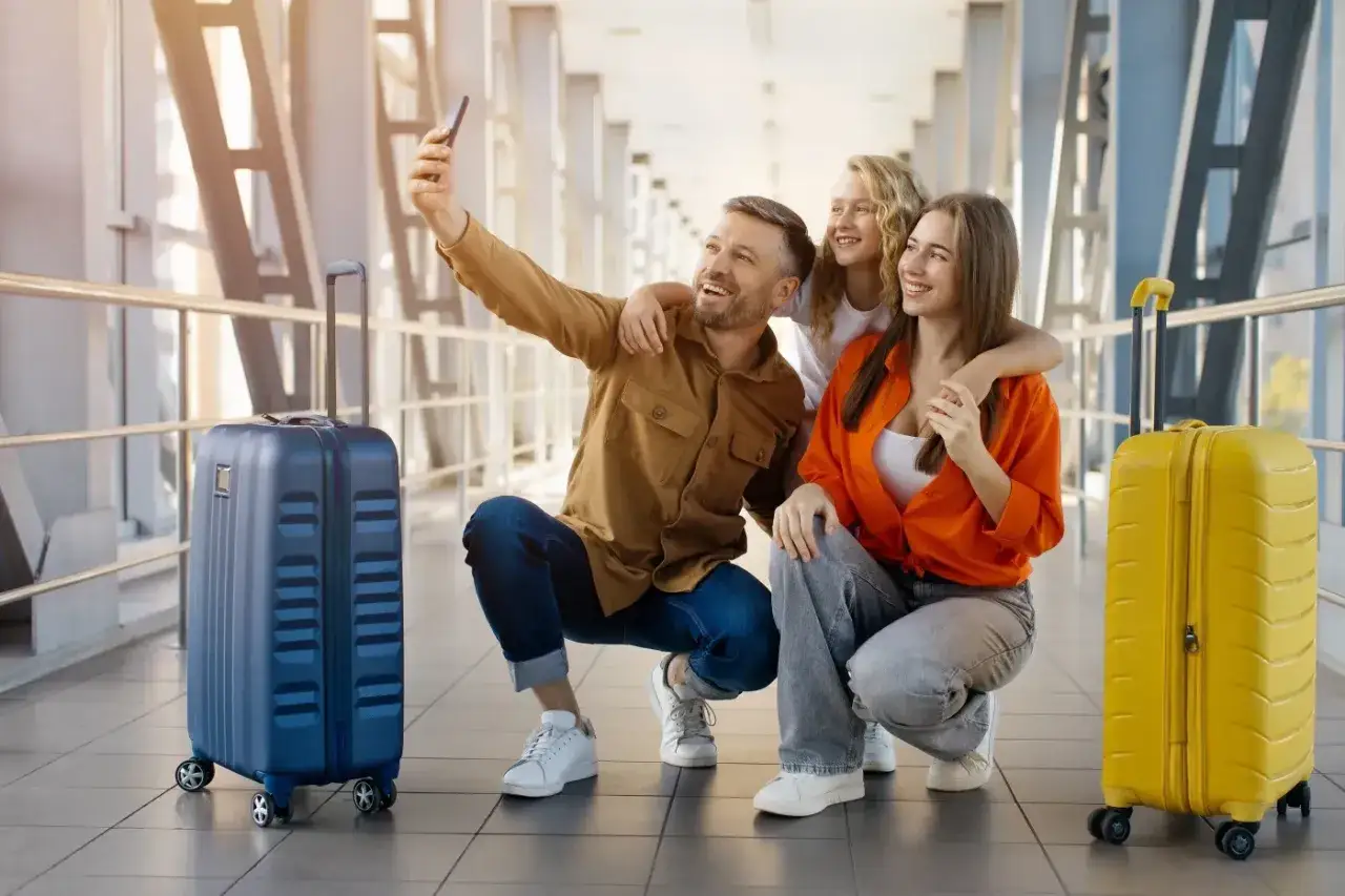 Rodzina robi selfie na lotnisku, obok walizek. Mimo obaw o overbooking, podróżują z uśmiechem.