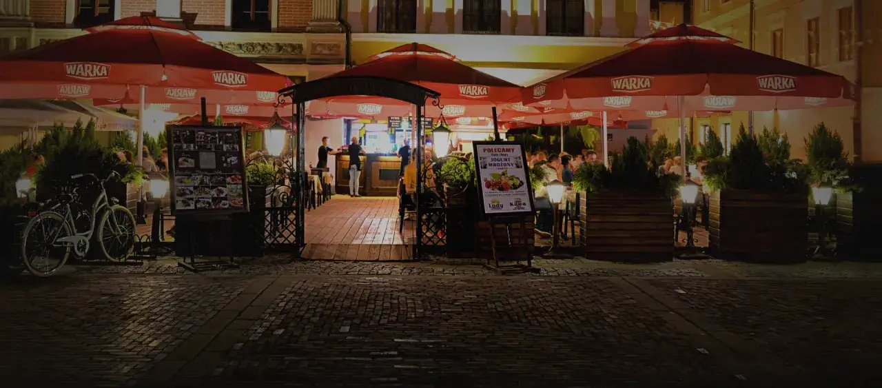 Wieczorne Zamość zaprasza do restauracji pod czerwonymi parasolami. Idealne miejsce, gdzie zjeść w Zamościu, z rowerami pod ścianą i menu pełnym pyszności.