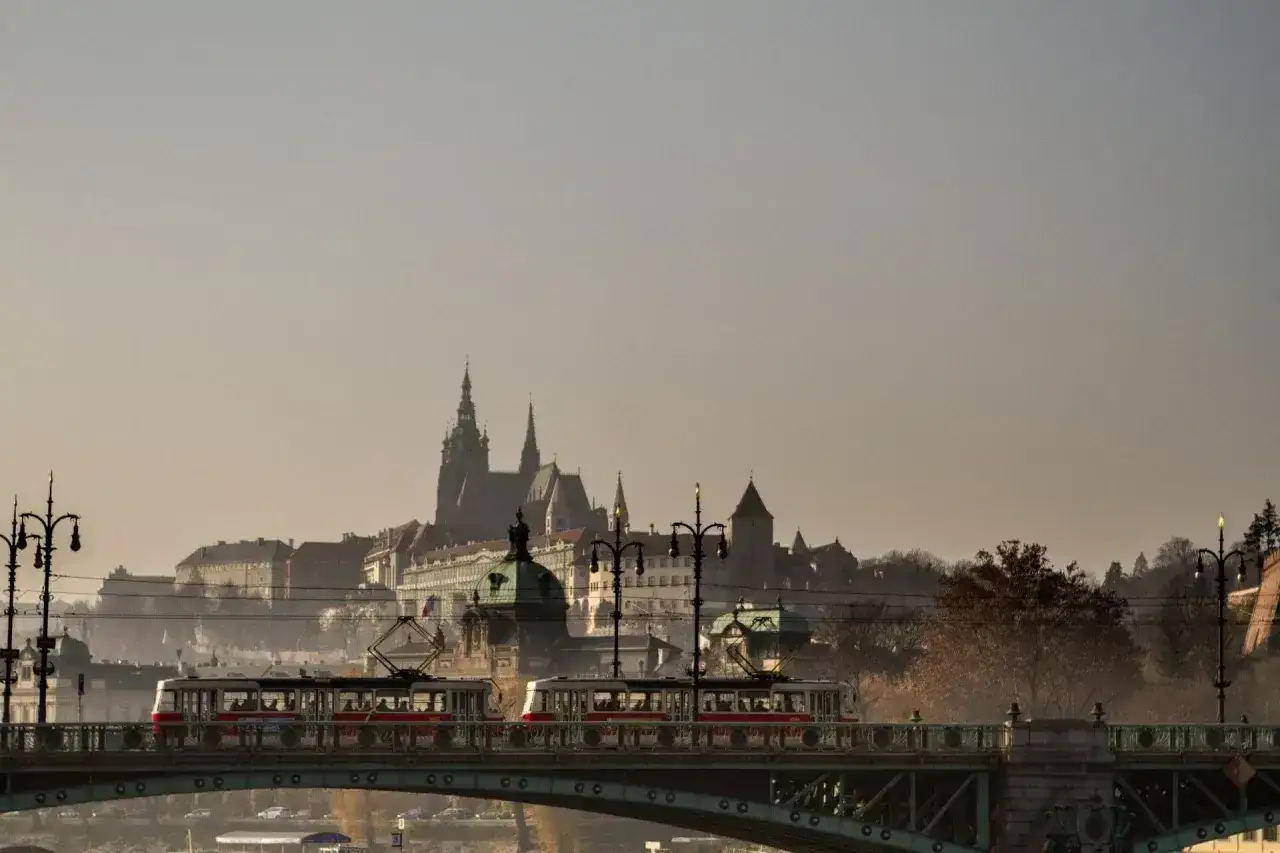 Tramwaje na moście w Czechach, z widokiem na praskie zamki i katedrę w oddali.