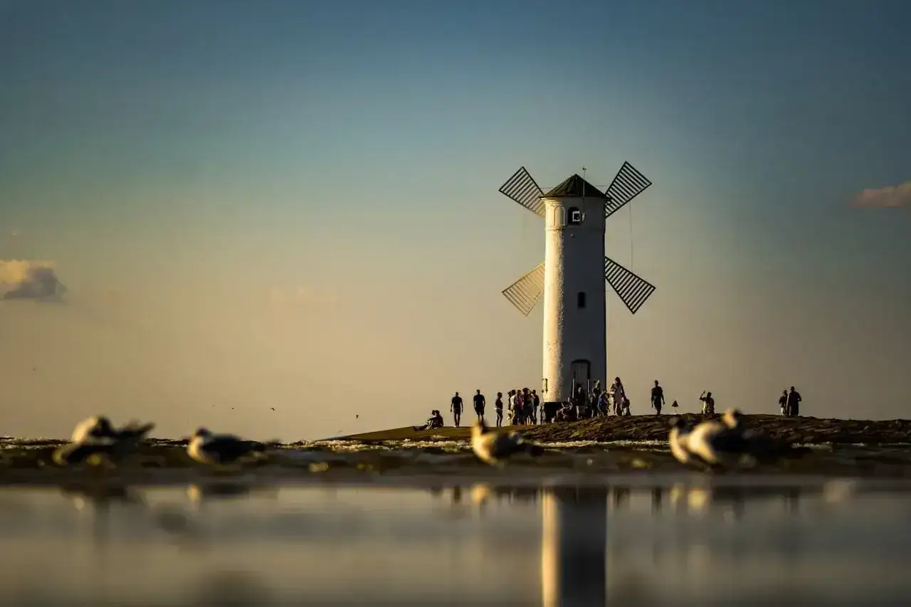 Biała latarnia morska w kształcie wiatraka, jedna z głównych promenada Świnoujście atrakcje, na tle zachodzącego słońca.