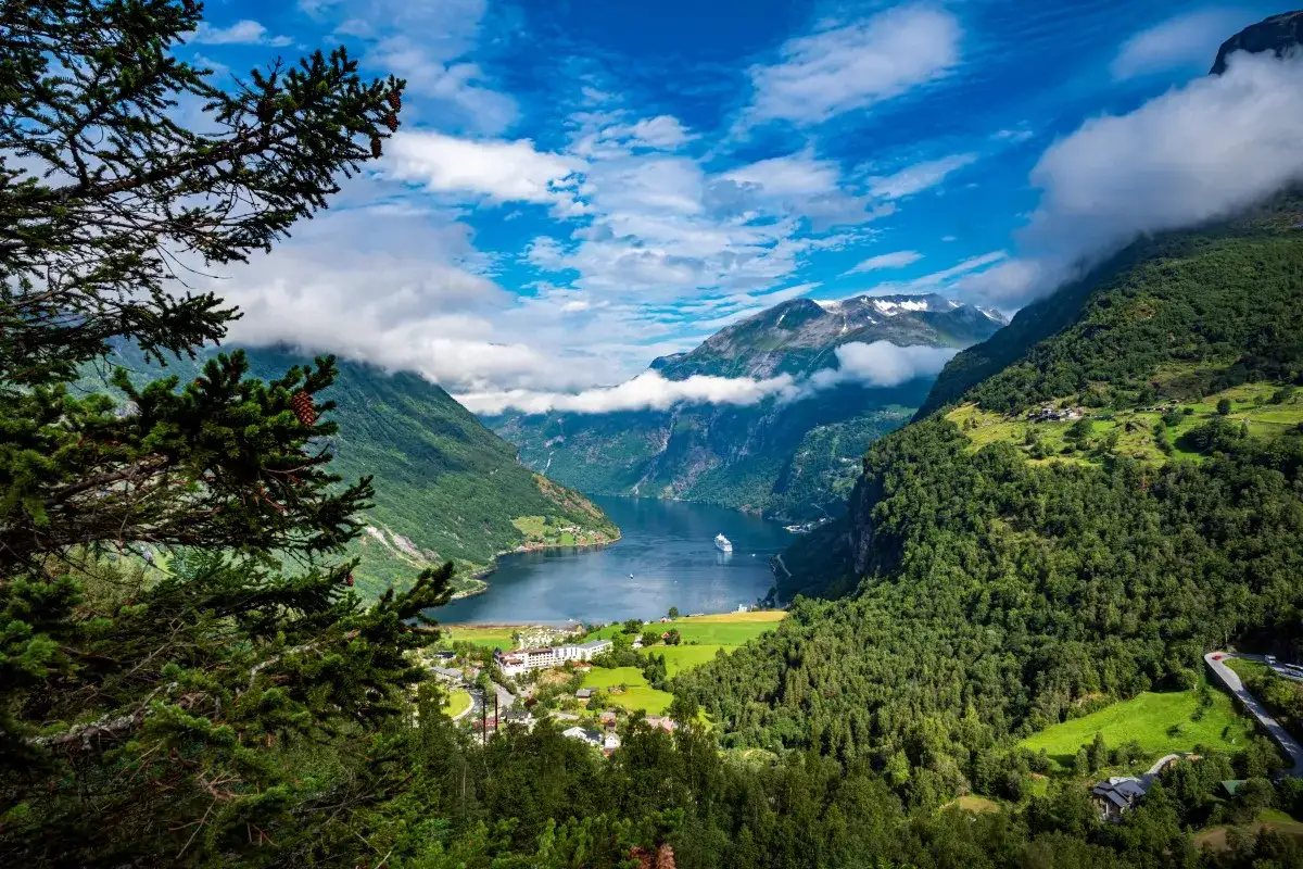 Widok na fiord podczas wycieczki do Norwegii. Statek wycieczkowy sunie po spokojnej wodzie, otoczonej zielonymi górami i malowniczą wioską.