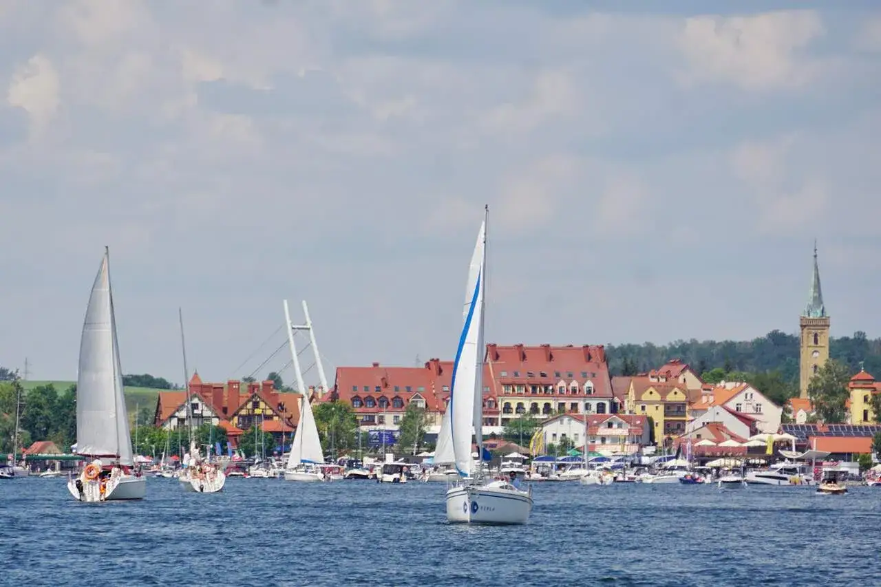 Żaglówki na jeziorze przy malowniczej miejscowości. Mikołajki co warto zobaczyć? Urokliwa panorama z portem i zabytkową wieżą.