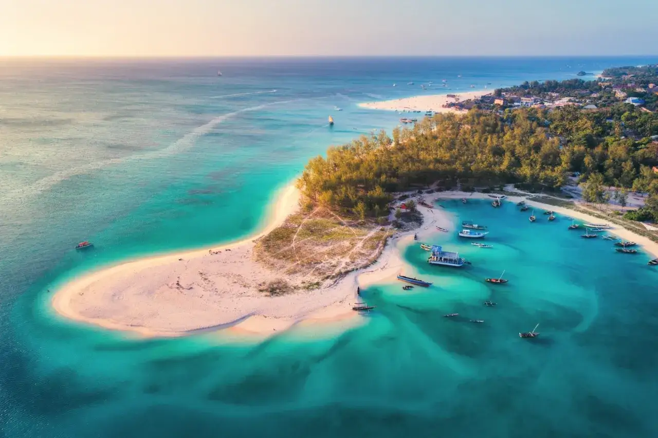 Rajska plaża na Zanzibarze, turkusowa woda, łodzie i palmy. Marzysz o podróży? Sprawdź, ile się leci na Zanzibar!