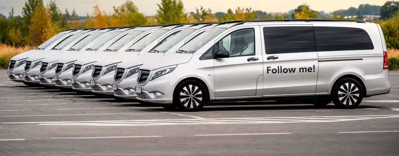 Rząd srebrnych vanów gotowych na transfer lotniskowy. Na jednym z nich napis 