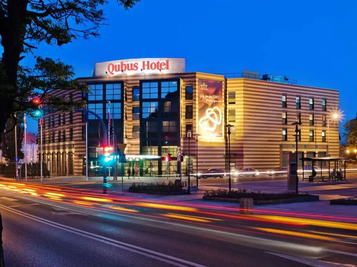 Nowoczesny hotel Qubus Hotel Gorzów nocą, z rozmazanymi światłami samochodów na ulicy.