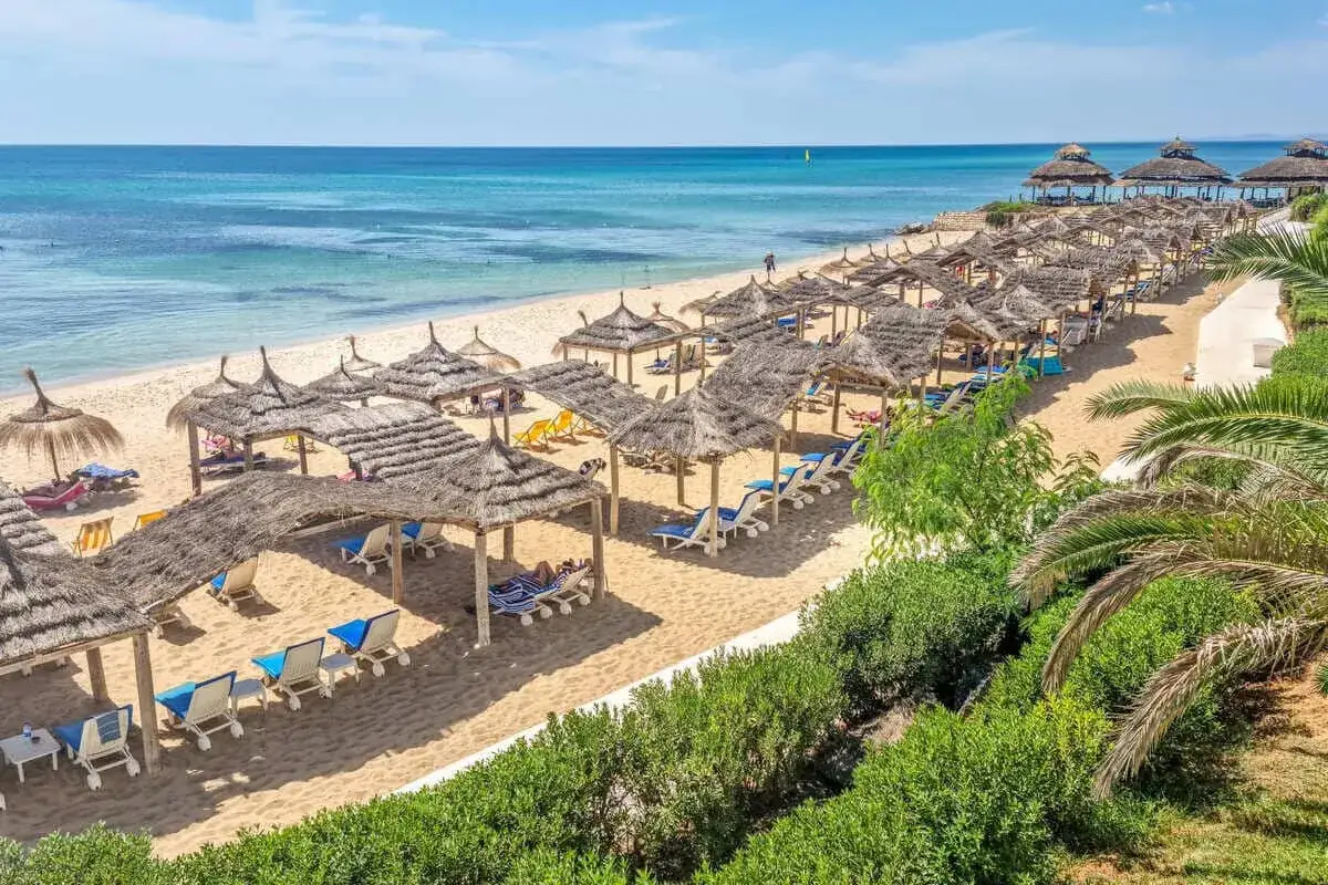Piękna plaża w Tunezji, idealna na lipiec. Słoneczna pogoda, turkusowe morze, leżaki pod strzechą.