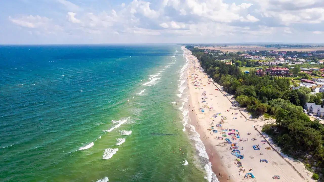 Słoneczny dzień na plaży w Sarbinowie nad morzem. Tłumy plażowiczów, kolorowe parawany i zielone morze Bałtyku tworzą letni krajobraz.