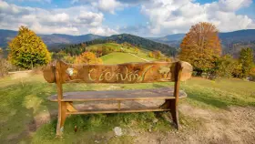Drewniana ławka z napisem "Ciechocinek" na tle jesiennych gór i zielonych wzgórz. Widok na Beskid Sądecki.