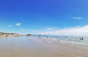 Słoneczna triest plaża piaszczysta z turkusową wodą i błękitnym niebem. Ludzie kąpią się i relaksują.