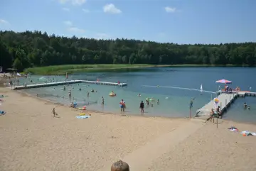 Słoneczny dzień nad jeziorem płotki. Ludzie kąpią się, pływają na dmuchanych zabawkach i odpoczywają na piaszczystej plaży.