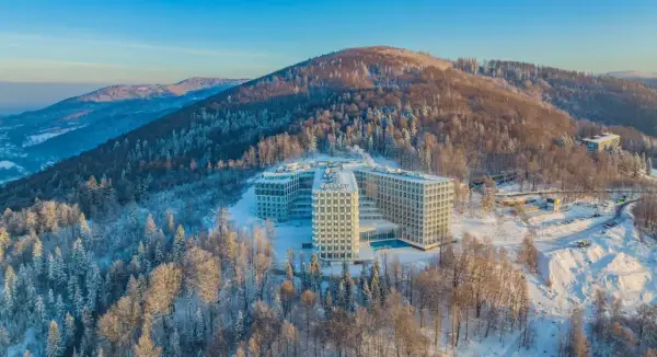 Nowoczesny hotel Crystal w zimowej scenerii, otoczony ośnieżonym lasem. To idealne miejsce na wypoczynek w Wiśle, górskim kurorcie.