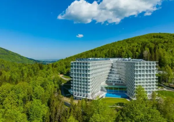 Nowoczesny Crystal Mountain Hotel Wisła otoczony zielonymi wzgórzami, z basenem i tarasami.