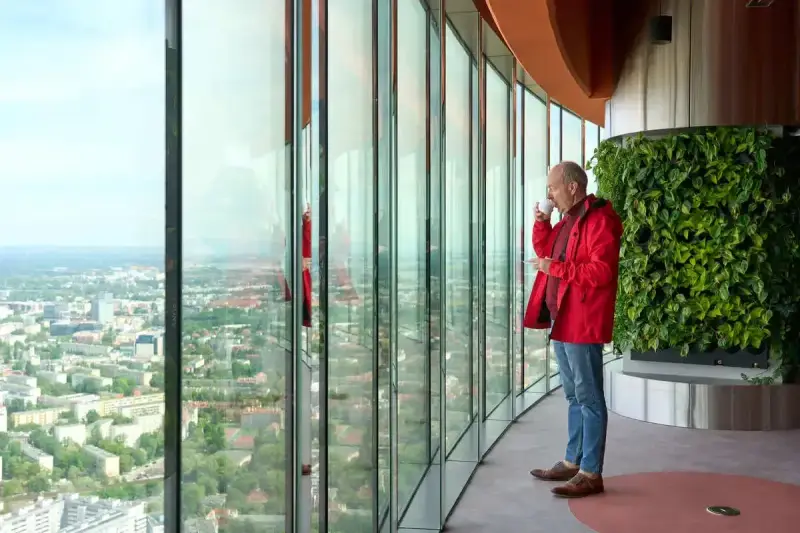 Mężczyzna pije kawę, podziwiając panoramę Wrocławia z tarasu widokowego. Sprawdź Sky Tower Wrocław cennik, by poznać ceny biletów.