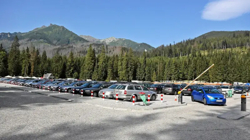 Parking przy wejściu na Morskie Oko. Rząd samochodów pod górskimi szczytami i gęstym lasem.