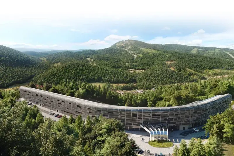 Nowy hotel w górach, o futurystycznym, zakrzywionym kształcie, otoczony gęstym lasem iglastym. W tle widać łagodne, zalesione wzgórza.